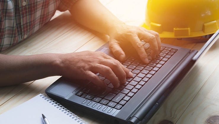 person typing on computer next to construction hard hat